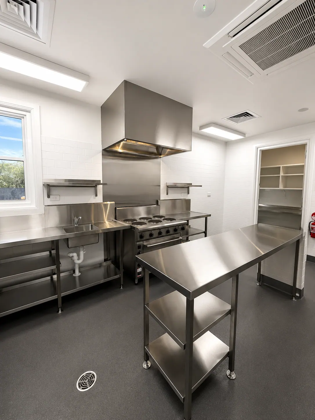 Commercial kitchen fitout with stainless steel benching, cooktop and exhaust hood